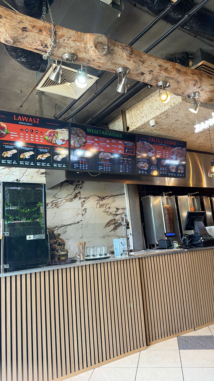 Lada lokalu z trzema ekranami menu i stanowiskiem kasowym przy rożnie